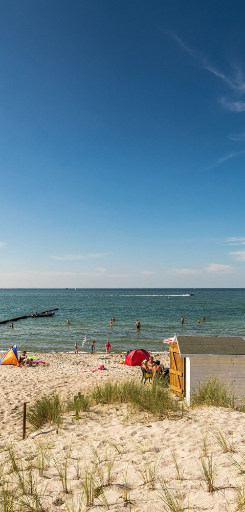 Strand von Baltic Freizeit in Markgrafenheide mit Badegästen, Sonnenschirmen und klarem blauen Himmel.