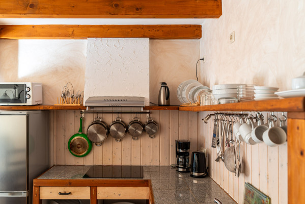 Voll ausgestattete Küchenzeile mit Mikrowelle, Herd, Geschirr, Kaffeemaschine und Hängeutensilien in einer Unterkunft von Baltic Freizeit in Markgrafenheide.