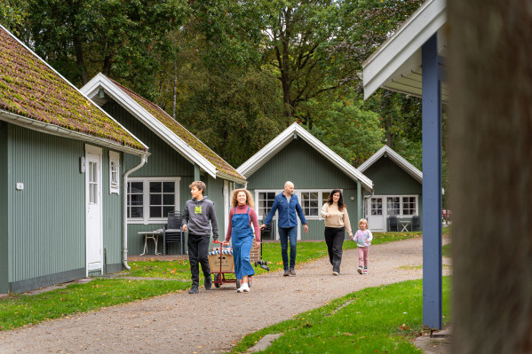 Familie spaziert zwischen grünen Hütten auf dem Campingplatz von Baltic Freizeit.