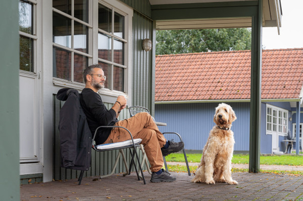 Ein Mann entspannt auf einer Terrasse mit seinem freundlichen, flauschigen Hund im Campingplatz Baltic Freizeit in Markgrafenheide.