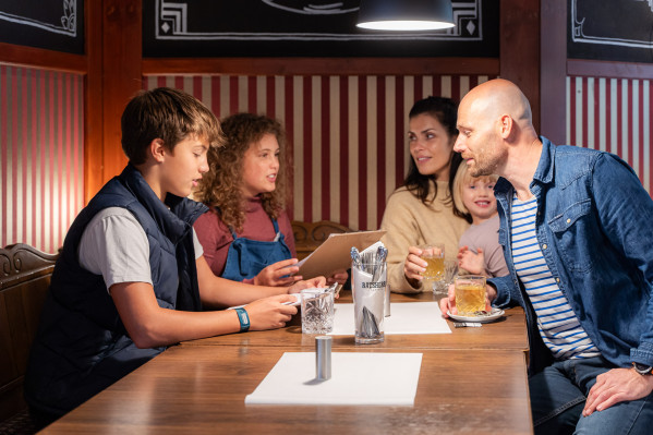 Familie mit drei Kindern in gemütlicher Ecke vom Restaurant wählen Speisen von der Karte aus.