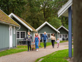 Familie spaziert zwischen grünen Hütten auf dem Campingplatz von Baltic Freizeit.